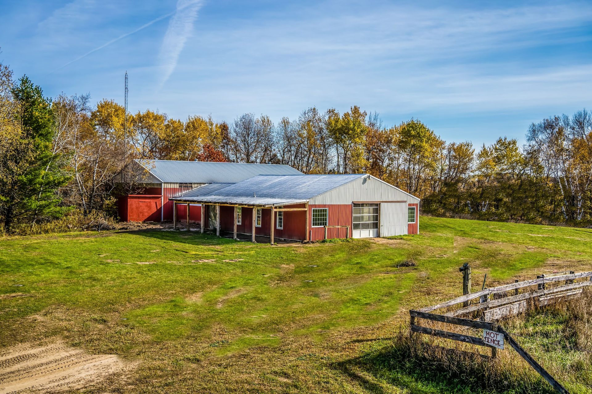 The red barn at The Lillian Fields sits on open rolling grounds in an autumn Minnesota field, framed by a weathered wooden fence and a treeline of gold and green.